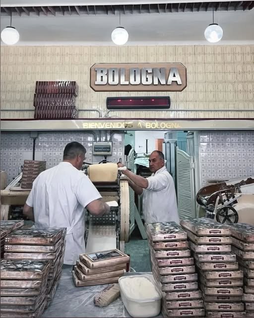 Interior del local: el cartel Bologna y dos personas trabajando la masa en la máquina